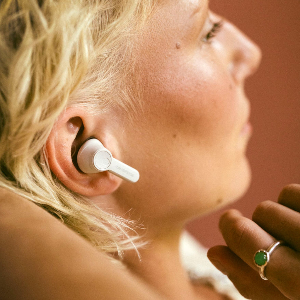 Woman wearing Cambridge Audio Melomania A100 SE earbud, close-up, White